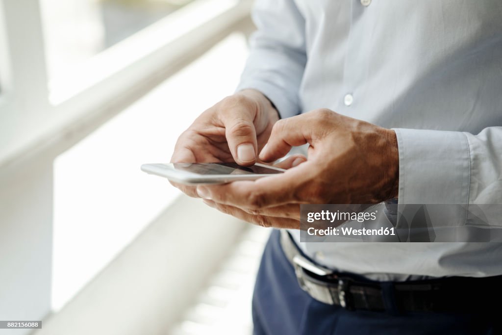 Close-up of businessman at the window using cell phone