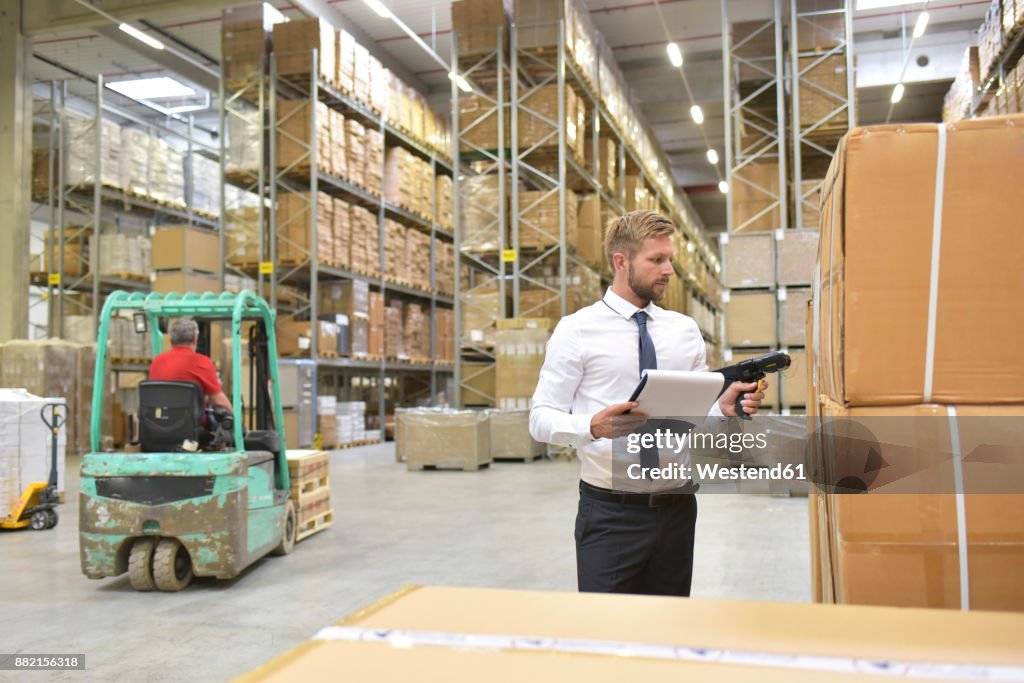 Businessman with clipboard in warehouse scanning goods