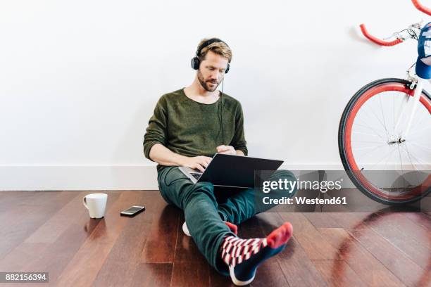 man with headphones sitting on the floor at home using laptop - school stockings stock pictures, royalty-free photos & images