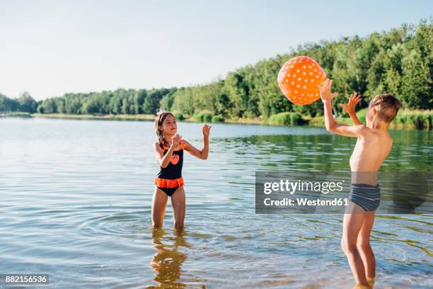 boy and girl standing at lakeshore playing with beach ball - german film ball stock-fotos und bilder