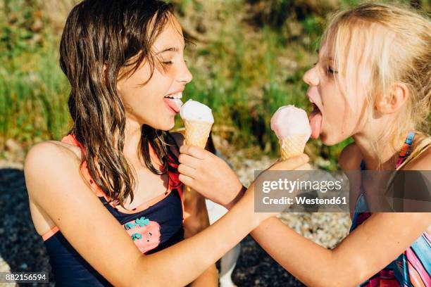 two girls eating icecream on the beach - tween girl swimsuit stock-fotos und bilder