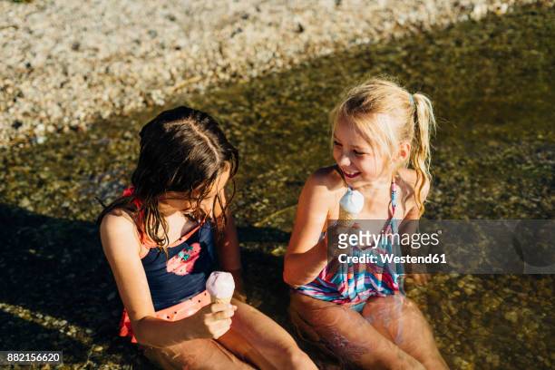 two girls sitting in water at lakeshore eating icecream - icecream beach stock pictures, royalty-free photos & images