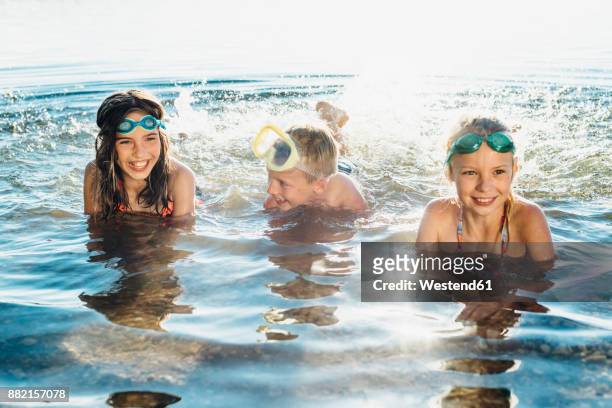 three smiling friends splashing with water at lakeshore - children only stock-fotos und bilder