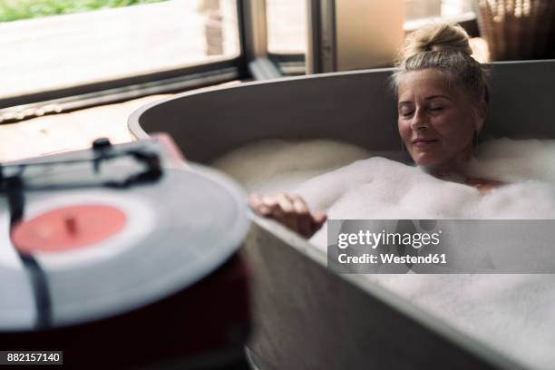 mature woman taking bubble bath, listening music from analogue record player - bathtub stock-fotos und bilder