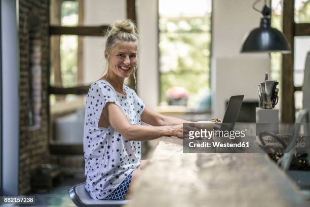 woman sitting in kitchen, using laptop - woman portrait kitchen laptop stock-fotos und bilder