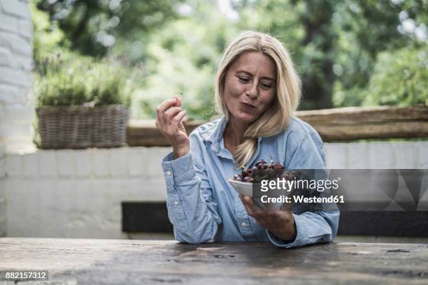 mature woman sitting on terrace - kirschen tisch weiß stock-fotos und bilder