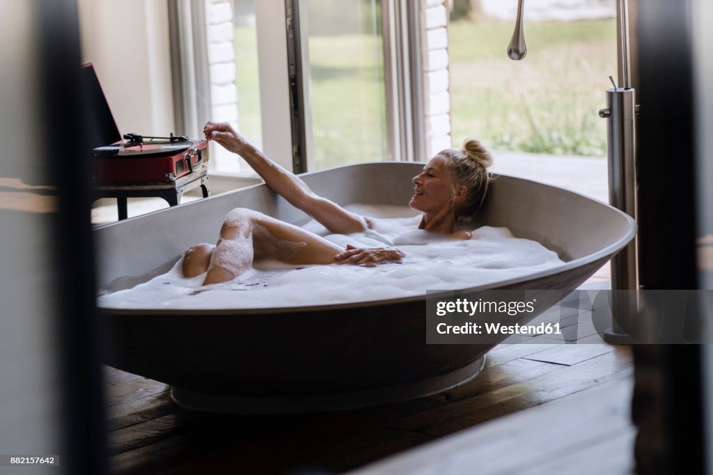 Mature woman taking bubble bath, listening music from analogue record player