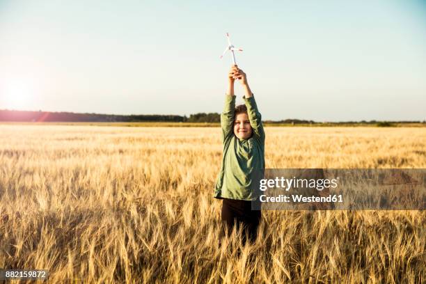 girl standing in grain field holding miniature wind turbine - small wind turbine stockfoto's en -beelden