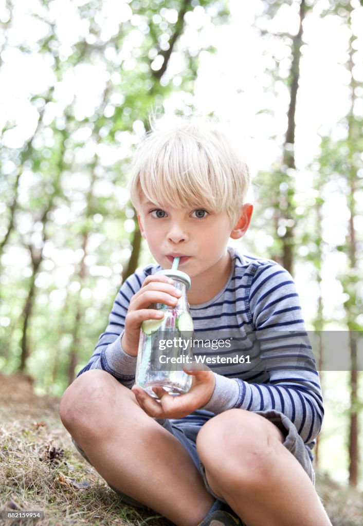 Boy drinking from glass of infused water in forest