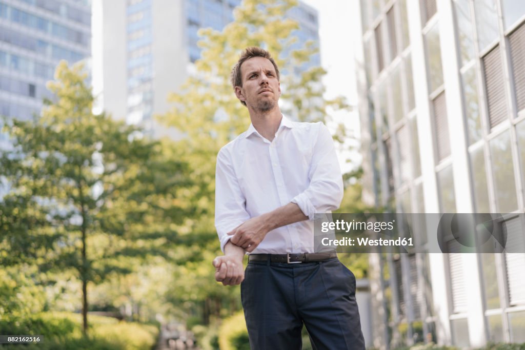 Portrait of confident businessman in the city rolling up his sleeves