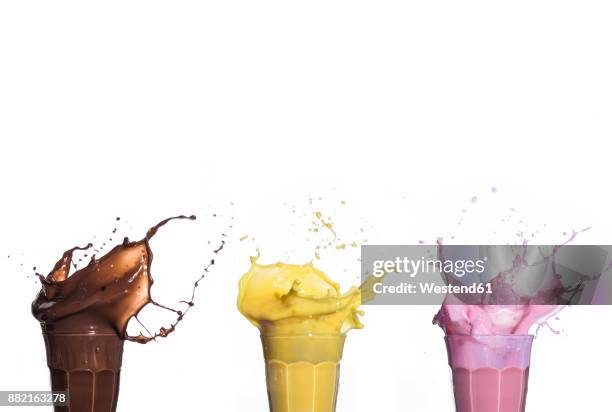 shakes of different flavors exploding on white background - milk shake stock-fotos und bilder