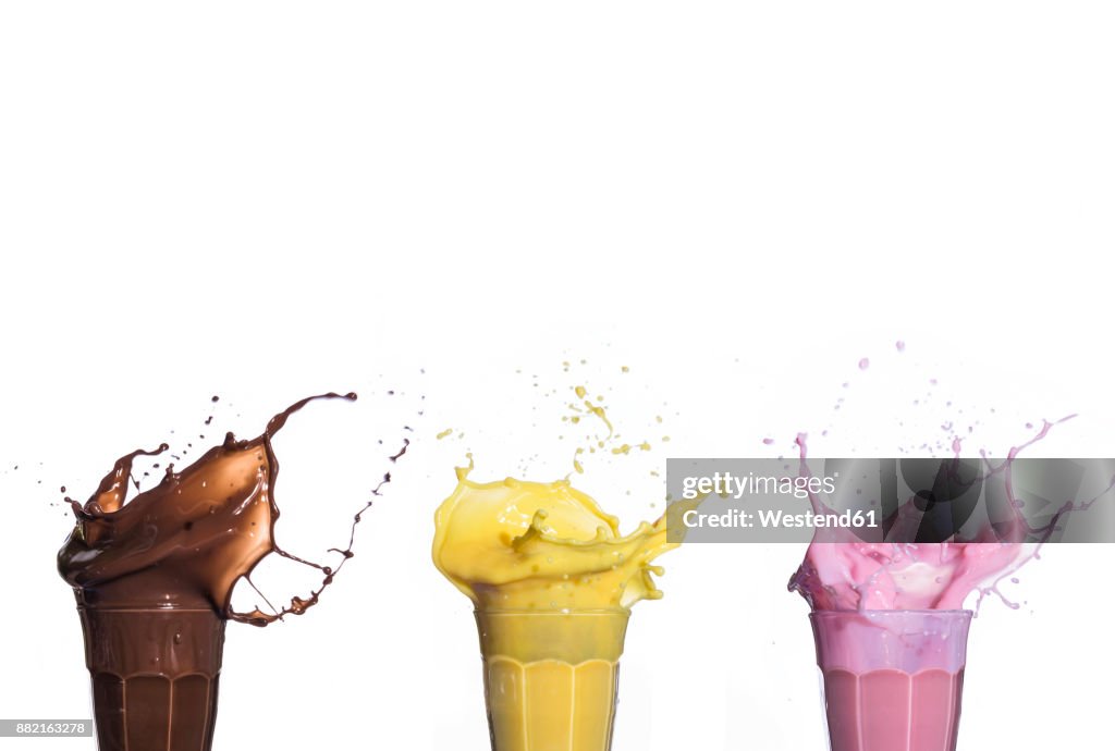 Shakes of different flavors exploding on white background