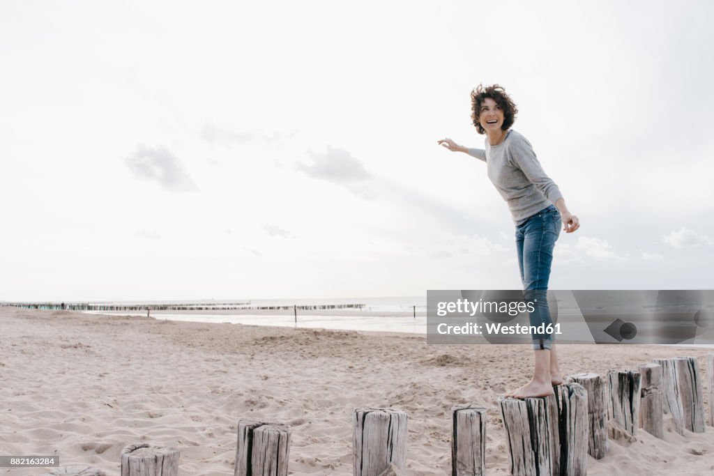 Happy woman balancing on wooden stake on the beach