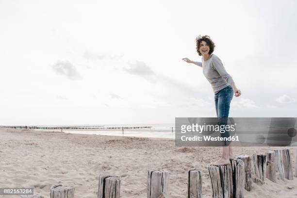 happy woman balancing on wooden stake on the beach - gender balance stock pictures, royalty-free photos & images