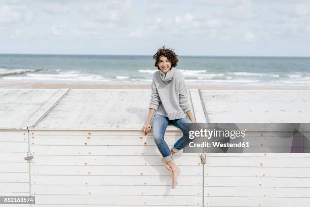 smiling woman sitting on wooden box on the beach - tossing hair facing camera woman outdoors stock pictures, royalty-free photos & images