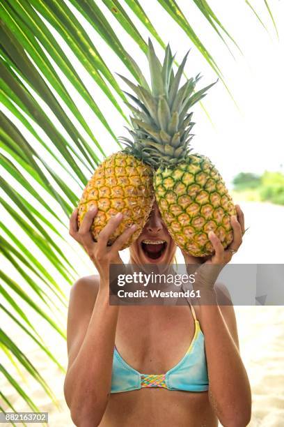 young woman holding two pineapples at palm tree - holding two things stock pictures, royalty-free photos & images