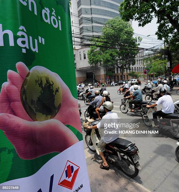Motorcyclists ride past a climate change awareness poster hunged on a tree on a main street in downtown Hanoi on June 5, 2009 on the occasion of the...