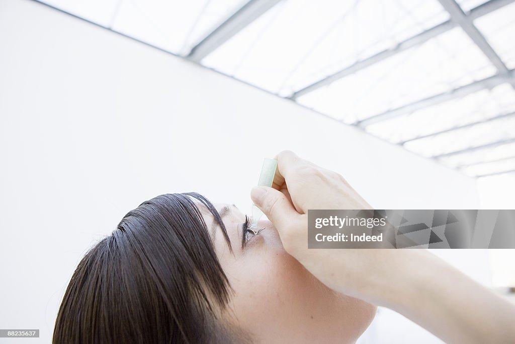 Young woman putting eye drops, side view