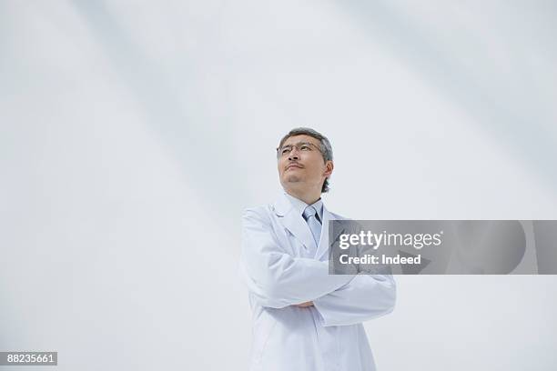 male doctor crossing arms, looking  up - doctors arms crossed stock pictures, royalty-free photos & images