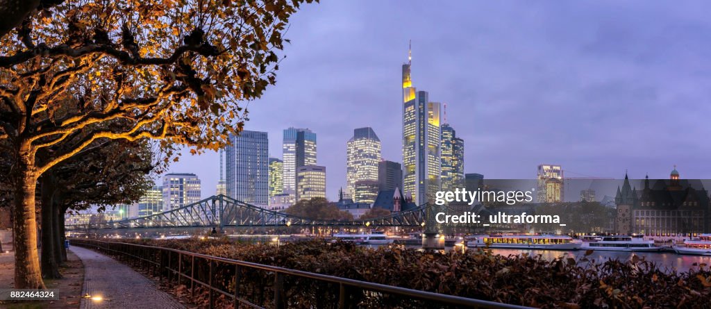 Panoramic view of the illuminated Frankfurt am Main skyline with Eiserner Steg from Schaumankai at dusk
