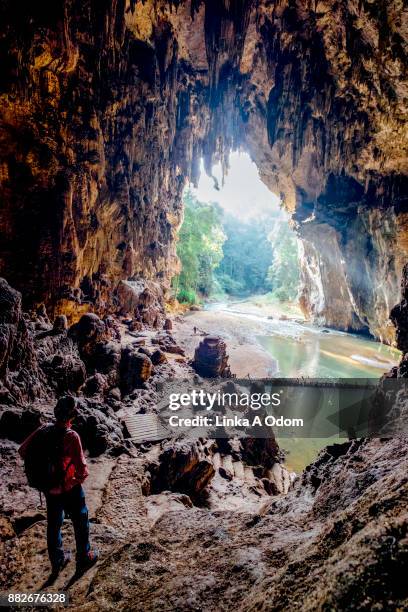 man looking at huge cave opening with river running through it - mae hong son provinz stock-fotos und bilder