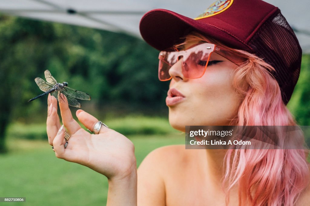 A Pretty Pink Haired Girl Blowing a Kiss to a Dragonfly on her Finger