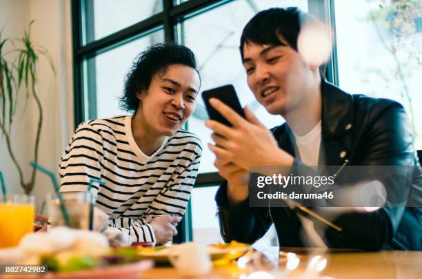 twee jonge man kijkend naar smartphone lachen - café cultuur stockfoto's en -beelden