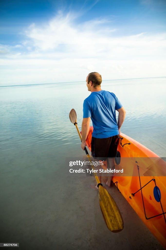 A man carrying a kayak into the ocean.