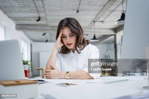 empresaria con dolor de cabeza sentado en el escritorio - mujer cansada fotografías e imágenes de stock