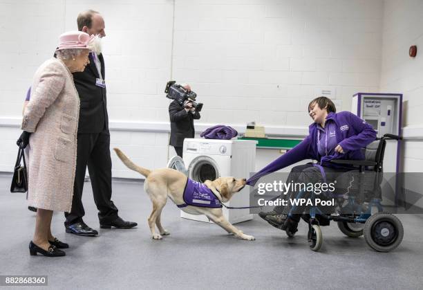 Queen Elizabeth II watches a demonstration by "Hettie" the Labrador dog showing how she can help to undress a disabled owner as she tours the...