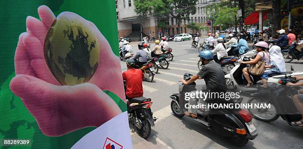 Motorcyclists ride past a climate change awareness poster hunged on a tree on a main street in downtown Hanoi on June 5, 2009 on the occasion of the...