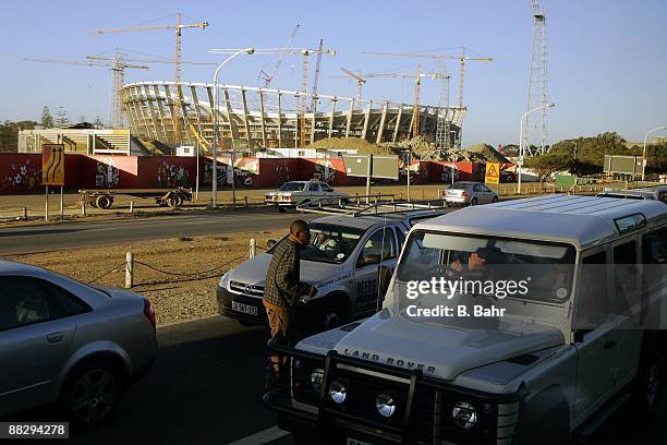 Beggar walks between luxury cars as cranes work on the construction of Green Point Stadium on March 17, 2009 in Cape Town, South Africa. South Africa...