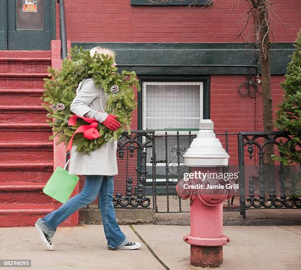 woman carrying christmas wreath on urban street - christmas tree stockfoto's en -beelden