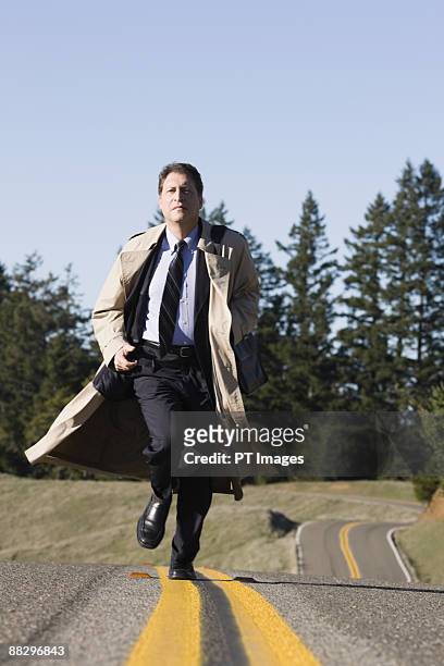 businessman running on remote road - trench coat stock pictures, royalty-free photos & images