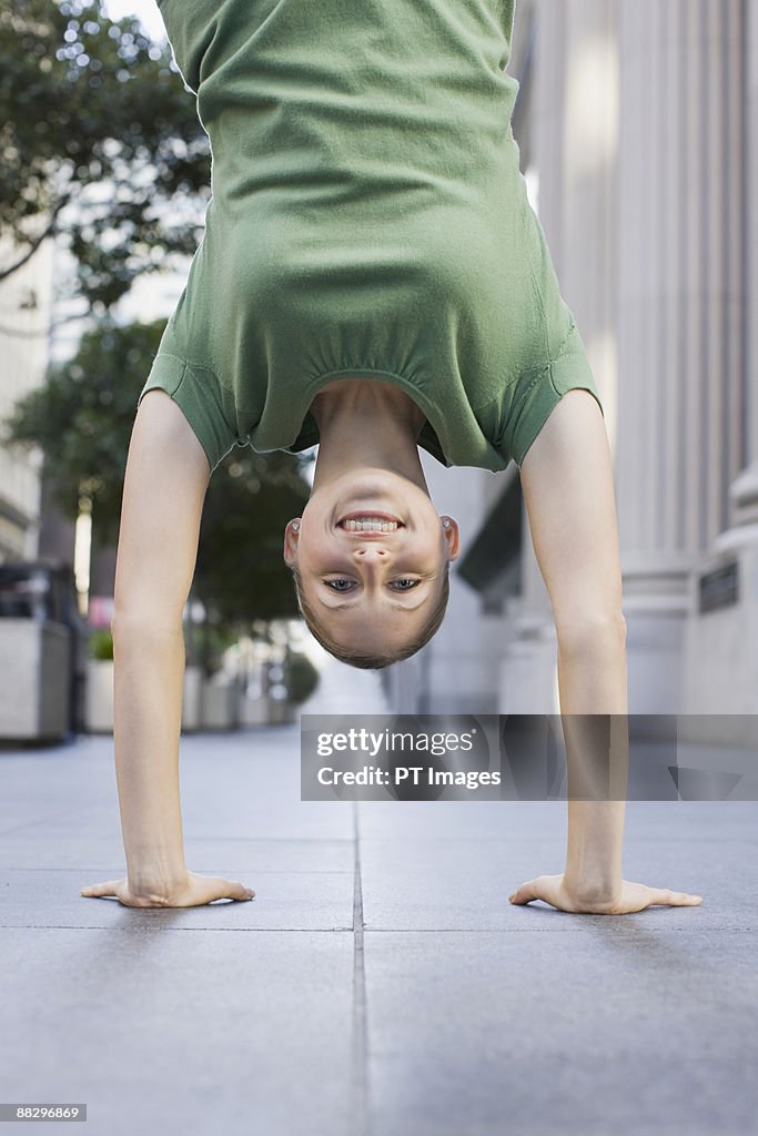 Businesswoman doing handstand on urban sidewalk