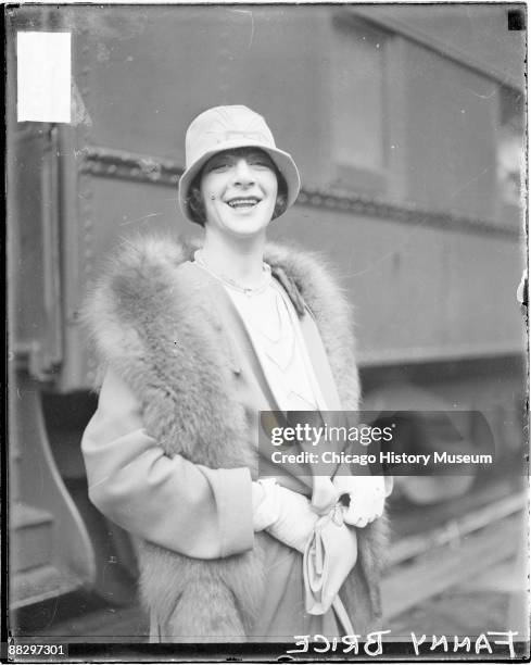 Three-quarter length portrait of Fanny Brice looking toward the camera, standing in front of a passenger train car in a railroad station in Chicago,...