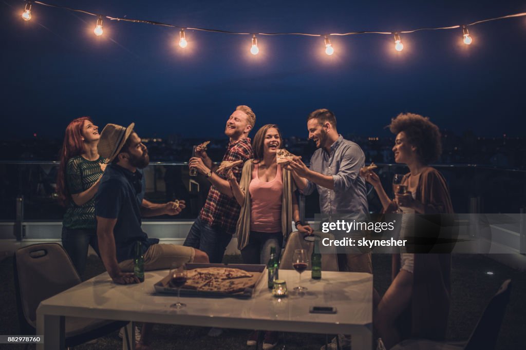 Amici gioiosi che cenano durante la notte su una terrazza.