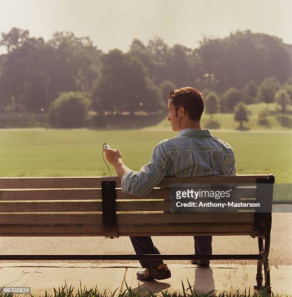 man listening to mp3 player on park bench - anthony masterson stock-fotos und bilder