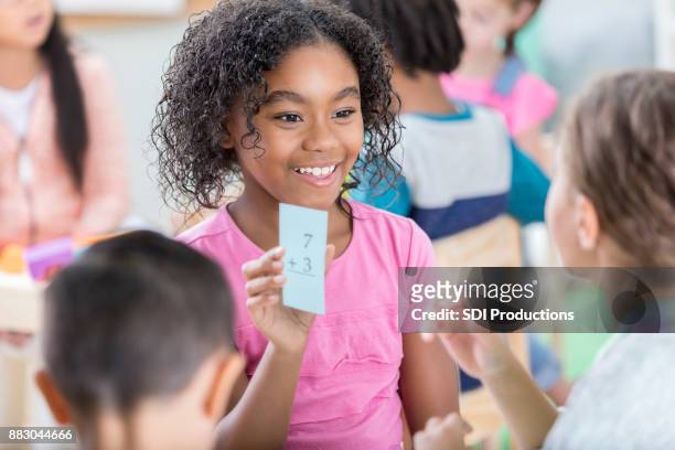 little girl holds up mathematics flash card to quiz friend - flash card stock pictures, royalty-free photos & images