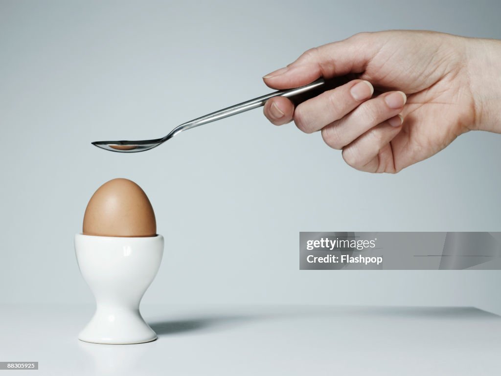 Hand with spoon and soft-boiled egg