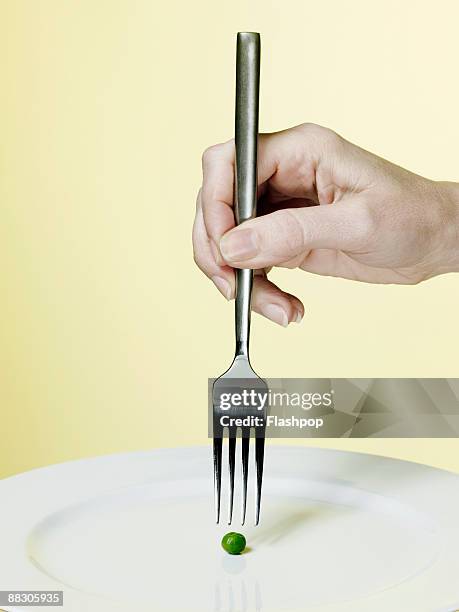 hand holding fork above a pea - fork stock-fotos und bilder