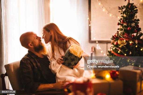 mature couple exchanging christmas gifts in front of christmas tree - christmas gift exchange stock pictures, royalty-free photos & images