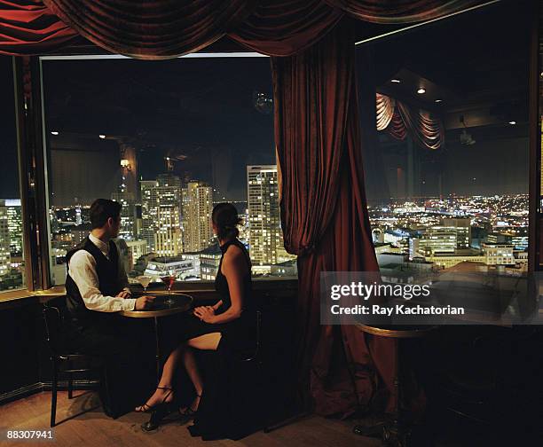 couple with cocktails overlooking cityscape - mirar por encima fotografías e imágenes de stock