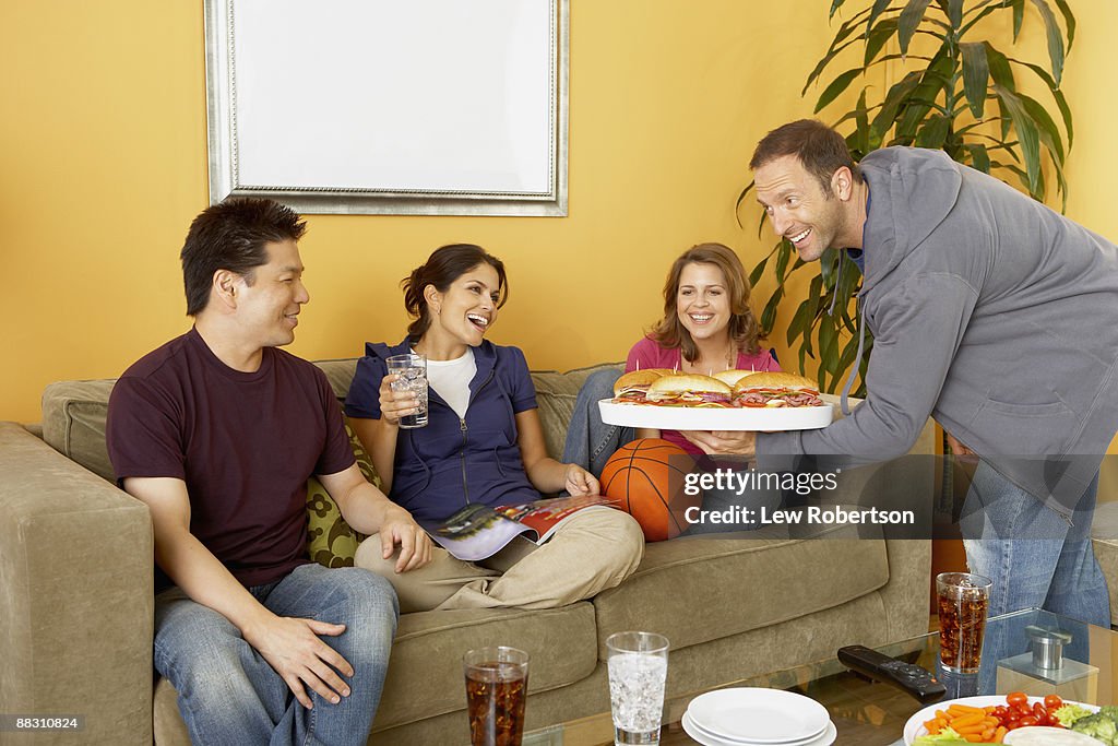 Man presenting platter of food to friends watching television