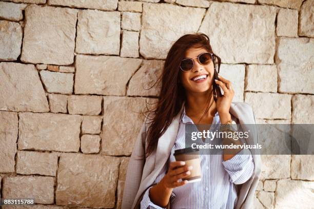 feliz mujer morena tomando café y hablando por teléfono - eurasia fotografías e imágenes de stock