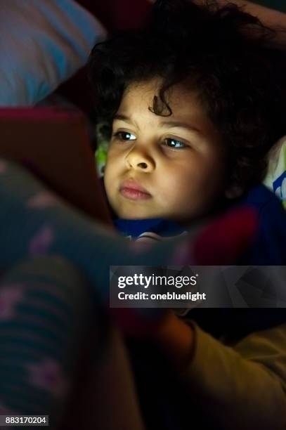 child (4-5) using digital tablet bedtime. - onebluelight stock pictures, royalty-free photos & images