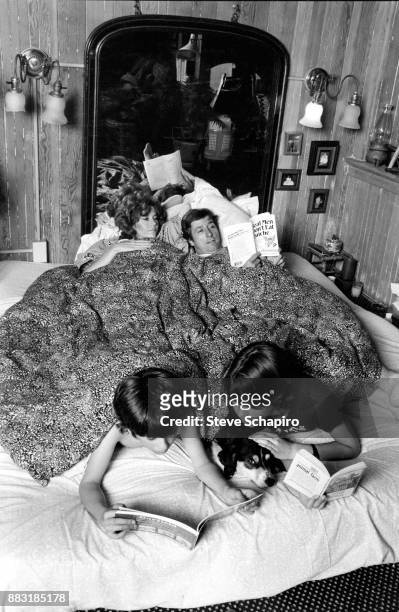 View of American married couple, actress Jane Fonda and politician and activist Tom Hayden , in bed, as the latter reads Bruce Feirstein's 'Real Men...