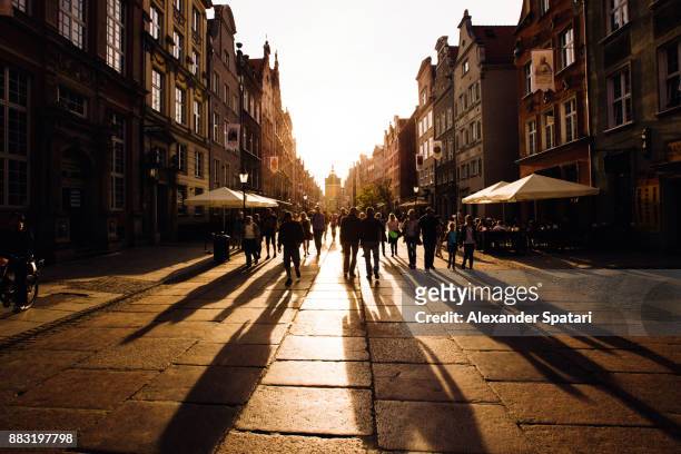 people walking towards the setting sun on an old city street - traffic free stockfoto's en -beelden
