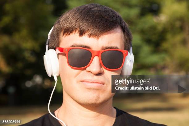 Mann mit weißen Kopfhörern und roter Sonnenbrille