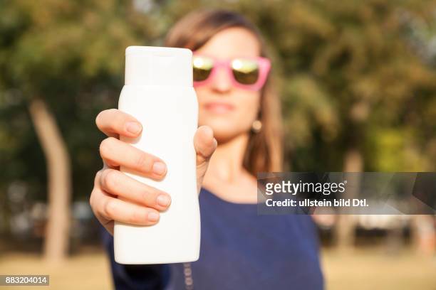Junge Frau mit Sonnenbrille hält Sonncreme Tube